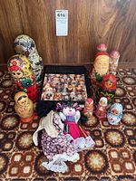 Photo showing collection of various nesting dolls of different sizes, two handmade fabric dolls, and a book titled 'Russian Matryoshka' on a patterned surface with wood background.