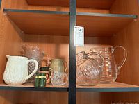 Seven assorted pitchers and jugs displayed on wood shelves with a range of materials and sizes.
