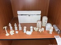 Front view of 15-piece Precious Moments nativity set with figurines and miniature buildings on a shelf next to a white box.