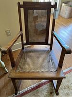 Front view of wooden rocking chair showing cane seat and backing with wooden frame.