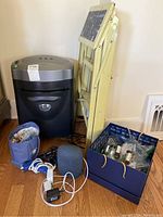 Royal paper shredder, yellow folding step ladder, Google Nest smart speaker, blue container with batteries and glue tools, and cords on wooden floor.