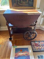Side view of the wooden tea trolley showing the pull-up sides closed and a decorative large wheel on the side.
