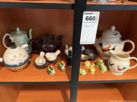 Shelf with collection of ceramic teapots and various animal-themed salt & pepper shakers including Humpty Dumpty, dark brown and floral rooster teapots, along with bird, strawberry, snail, turtle, and frog shakers.