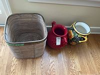 Photo shows two ceramic urns, one red with handles and one decorated with sunflowers, alongside a large wicker basket.