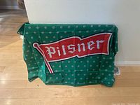 Green Pilsner flag displayed draped over surface with small white emblems and red banner with 'Pilsner' text