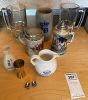 All drinkware and dice arranged on wooden surface showing variety of mugs, steins, sake bottle, shot measure, whiskey pitcher and dice