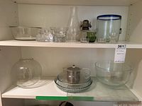 Shelf with various glassware including bowls, teapot with metal infuser, pie plate, oil lamp base, candle holders.