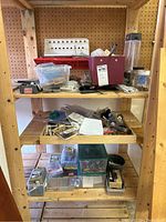 Wooden shelving with three shelves holding various hardware items including screws, nails, clamps, containers with small parts, and miscellaneous small tools.