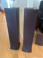 Full view of two black Polk tower speakers upright on floor with fabric grilles and rectangular angled bases.