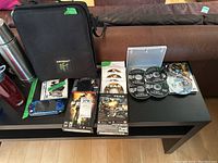 Black Nintendo 64 carrying case, blue Sony PSP console, various game cases and loose discs arranged on black table