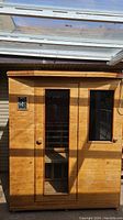 Exterior front view of wood-panel sauna with glass door and side window