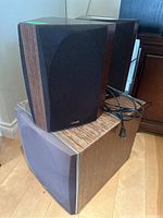 Three Polk Audio speakers together: two wood grain bookshelf speakers with black fabric covers on top of a larger horizontal speaker with gray fabric cover and wood grain top.