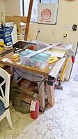 Front and side view showing table saw in garage setting with various items around including a fire extinguisher and boots below the table saw base.