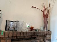 Photo of various glass vases, candles, candle holders, and framed art on a mantelpiece showing contents of the lot and condition of items.