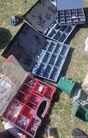 Four hardware organizer trays spread on grass showing bolts, nuts, washers, and wire harnesses