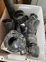 Box with assorted ABS plumbing fittings in various sizes and types including elbows, coupling, reducer and flange fitting.