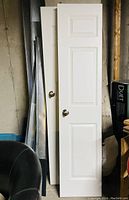 Two white bi-fold doors standing vertically against a wall, each with a metallic round knob attached. The doors have a panel design and appear clean with no visible damage.