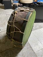 Full side view of the drum showing the brown wood body, rope tension cords, and worn condition.