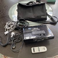 Epson projector next to VGA and audio cables and a black Epson carrying case on a round table.