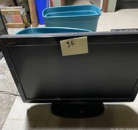 Front view of Sharp AQUOS 32-inch LCD TV showing screen and base stand, black frame with post-it note labeled '32'.