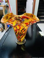 Image of the colorful glass vase showing the flared rim and multicolored speckled pattern with dominant yellow, red, black and blue colors.