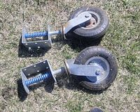 Two heavy duty caster wheels with attached blue coil springs and metal mounting brackets lying on grass, showing full view of wheels and shock absorbers
