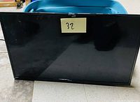 Full front view of the RCA 32-inch LED TV showing clean and undamaged screen with a sticky note labeled 32 on it.