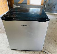 Closed front view of a Sylvania mini fridge with stainless steel door and black top.