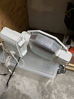 White metal grow light with reflector and cord, placed on plastic container in a room with wood paneling and concrete floor.