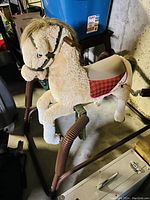 Side view of tan plush ride on horse mounted on brown metal frame with spring coils, showing saddle and reins.