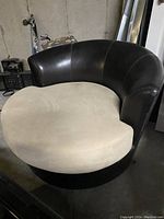 Front view of round love seat showing beige suede-like seat cushion and dark brown faux leather backrest and base.