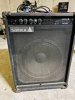 Front view of the Samick SM-50B bass amplifier showing control panel and large speaker grill.