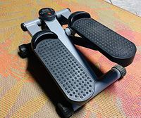 Front angled view showing textured black foot pedals, digital monitor, and metal frame of portable stair climber exerciser.