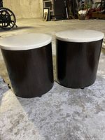 Two brown and white stools with cylindrical bases and round tops shown from an elevated angle to display side profile and size.