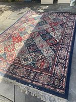 Full view of the large area rug laid out on pavement showing the overall pattern and fringe.