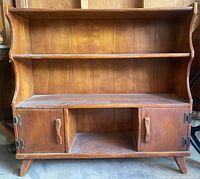 Front view of mid-century modern wooden bookcase showing two shelves, two lower cabinet doors with wood handles, tapered legs, and vertical wood plank back.