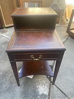 Front view of vintage mahogany telephone side table showing drawer with brass handles, lower shelf, overall condition, and wear on wood.