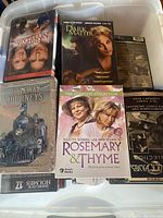 Plastic bin filled with assorted DVDs showing titles like Dark Matter, Rosemary & Thyme, and Railway Journeys