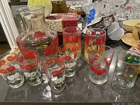 Photo of the entire lot arranged on a table including the decanter, various glasses with floral and cherry designs, and flat juice glasses.
