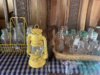 Wide view of vintage milk bottles arranged in metal and woven baskets with yellow oil lantern in front