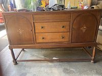 Full front view of the vintage wooden buffet showing 3 drawers with brass handles and 2 side cabinets with floral inlay decoration, standing on turned legs.
