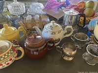 Image showing multiple teapots of various styles and materials, vintage creamer and sugar bowl with sterling silver overlay, and surrounding kitchen items.