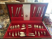 Full set of silver-plate flatware displayed in open wooden case with red velvet interior, showing knives, forks, spoons, and specialty utensils.