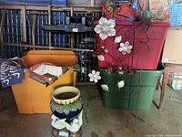 Wide view of lot showing majolica vase with doves on stand, orange bin filled with yard flags, and metal yard decorations leaning against storage containers