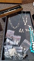 Full lot of jewelry including necklaces, earrings in plastic bags, brooches and rings on black background