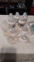 Tommee Tippee bottles with additional tops and nipples arranged on table showing condition and quantity