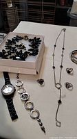 Long silver necklace with black bead accents, two bangle bracelets, three rings, and two wristwatches laid out on table.