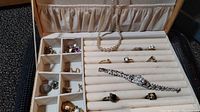 Jewelry holder filled with various rings, clip-on earrings, and a pearl necklace, showing the overall content and condition of the lot.