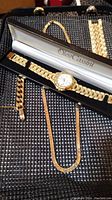 Overview of all items showing Oleg Cassini watch in box, gold chain, bracelet, and partial rings