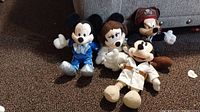 Four plush Disney characters on carpeted floor illustrating different themed costumes of Mickey and Minnie Mouse